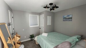A bedroom with a bed, a window, a painting, and a ceiling light fixture.