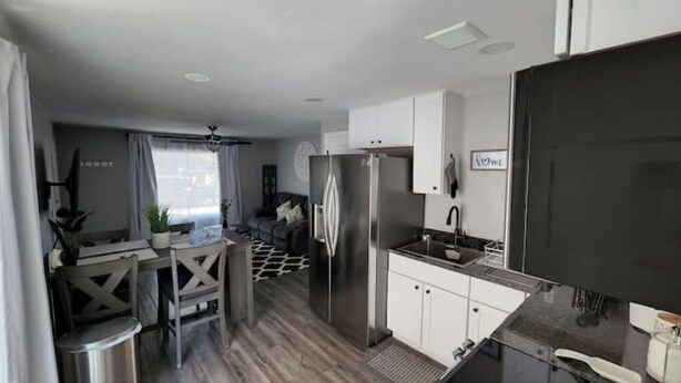 A compact kitchen with white cabinets, a stainless steel refrigerator, and a black countertop.
