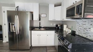 A modern kitchen with stainless steel appliances, white cabinetry, and a tiled backsplash.
