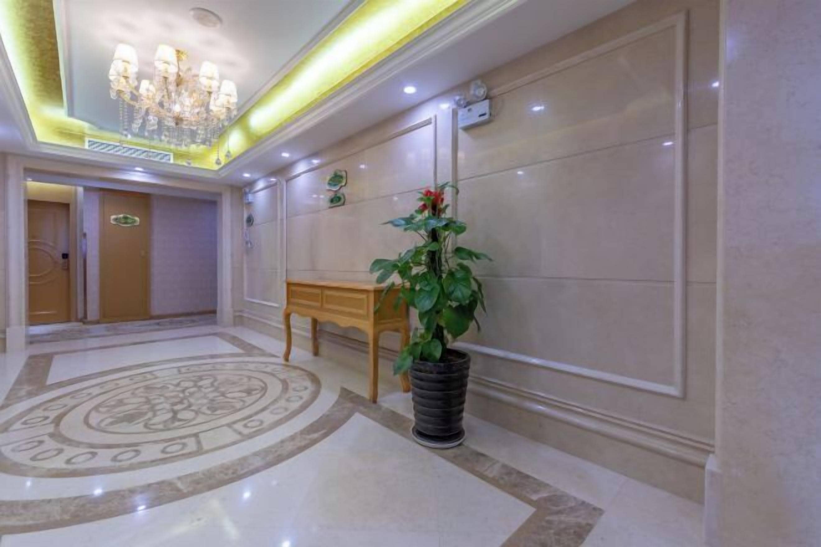A hallway with a chandelier, a potted plant, and a wooden table.