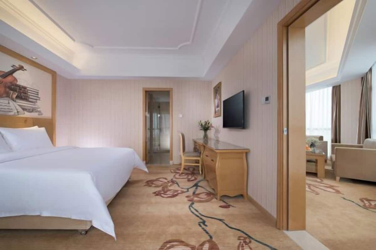 A hotel room with a bed, a desk, a chair, a television, and a door leading to another room.