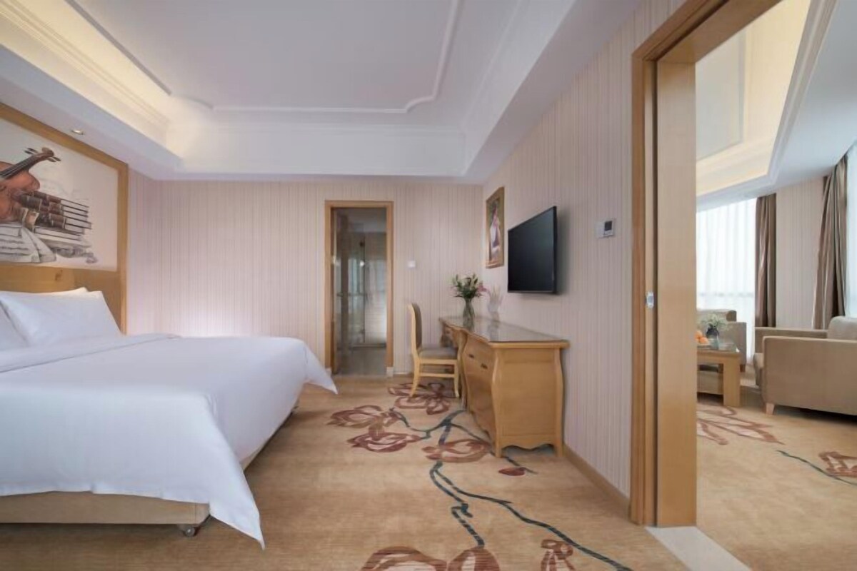A hotel room with a bed, a desk, a chair, a television, and a view of the outside.