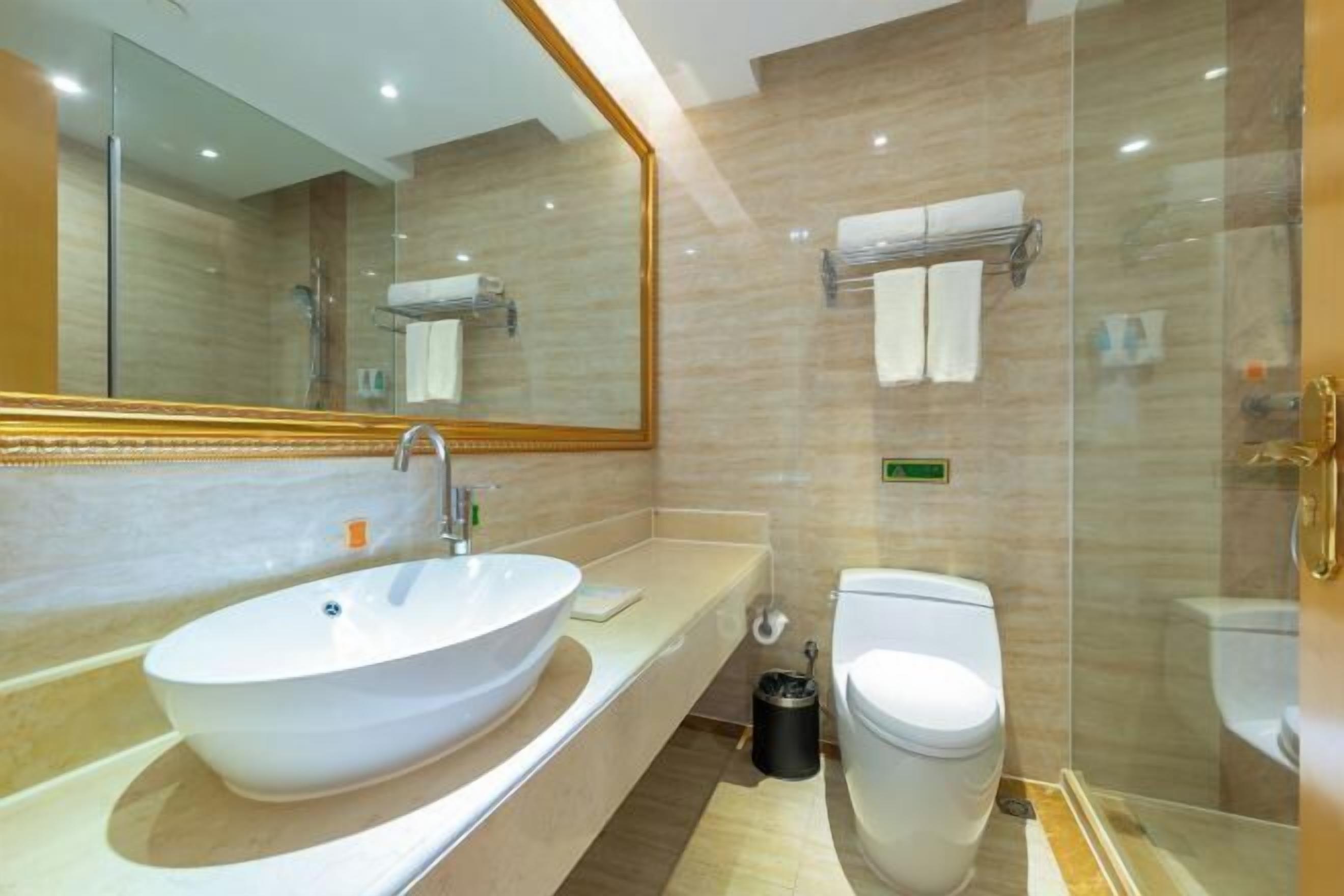 Un baño moderno con un lavamanos ovalado grande, un inodoro y una zona de ducha con mampara de vidrio.