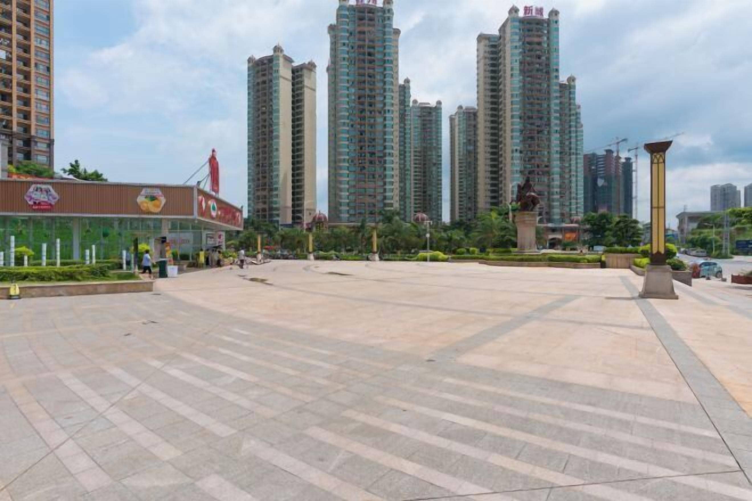 A spacious plaza with high-rise buildings in the background, a statue, and a restaurant with outdoor seating.