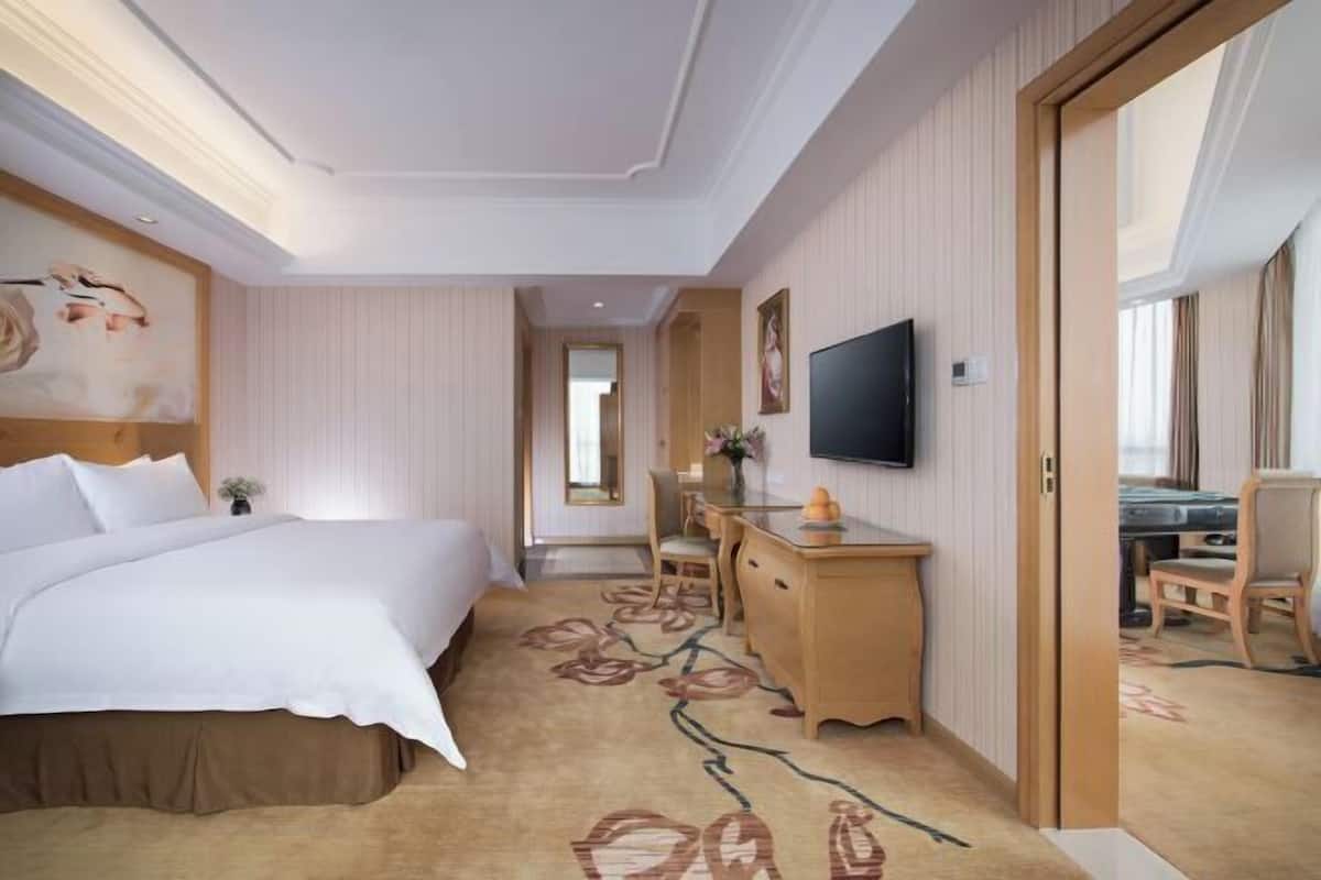 A hotel room with a bed, a desk, a television, and a view of the outside.