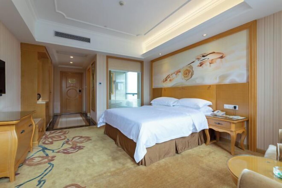 A hotel room with a bed, bedside table, and a large painting on the wall.