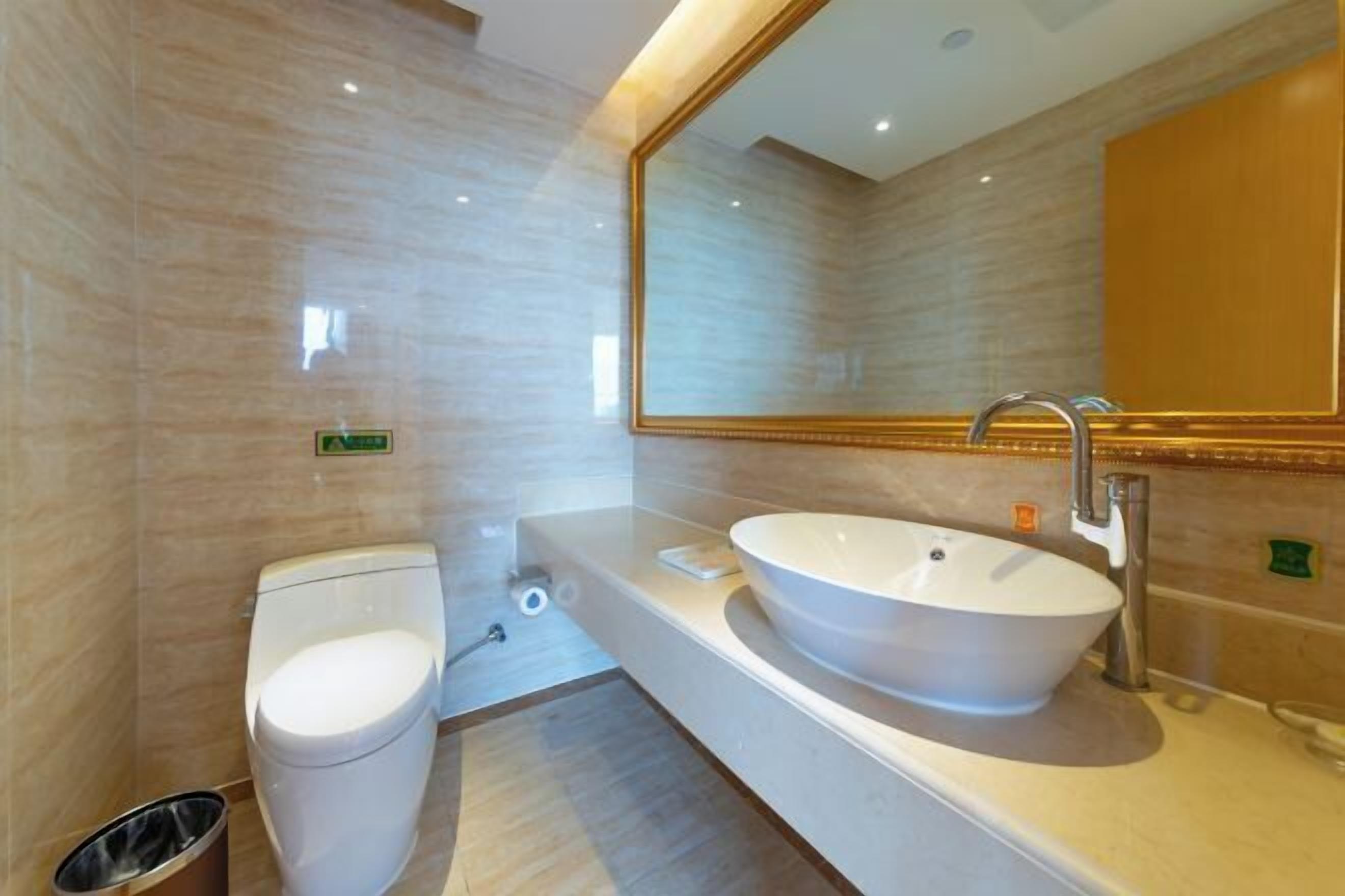 A modern bathroom with a white toilet, a large oval sink, and a mirror with a gold frame.