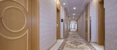 Un pasillo largo y estrecho con alfombra decorada y puertas de madera.