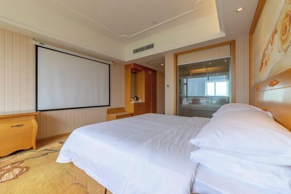 A hotel room with a large bed, a wooden nightstand, a projector screen, and a view of the outside through a glass door. - Vienna International Hotel (Yulin rongzhou bridge railway station shop ) (Rong County)