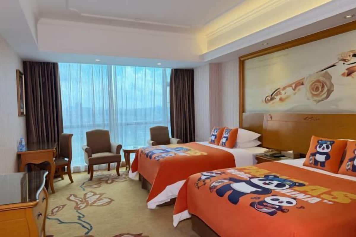 A hotel room with two beds, a desk, a chair, and a large window with curtains.