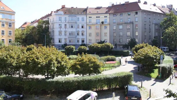 A multi-story building with a mix of architectural styles, surrounded by well-maintained greenery and a paved area with parked cars. - Cosy & Spacious Apartment, City Center, WiFi FREE (Hlavní mesto Praha)