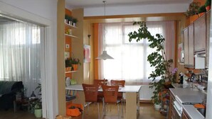 A spacious living area with a dining table and chairs, a kitchen with cabinets and appliances, and a large window with curtains. - Cosy & Spacious Apartment, City Center, WiFi FREE (Hlavní mesto Praha)