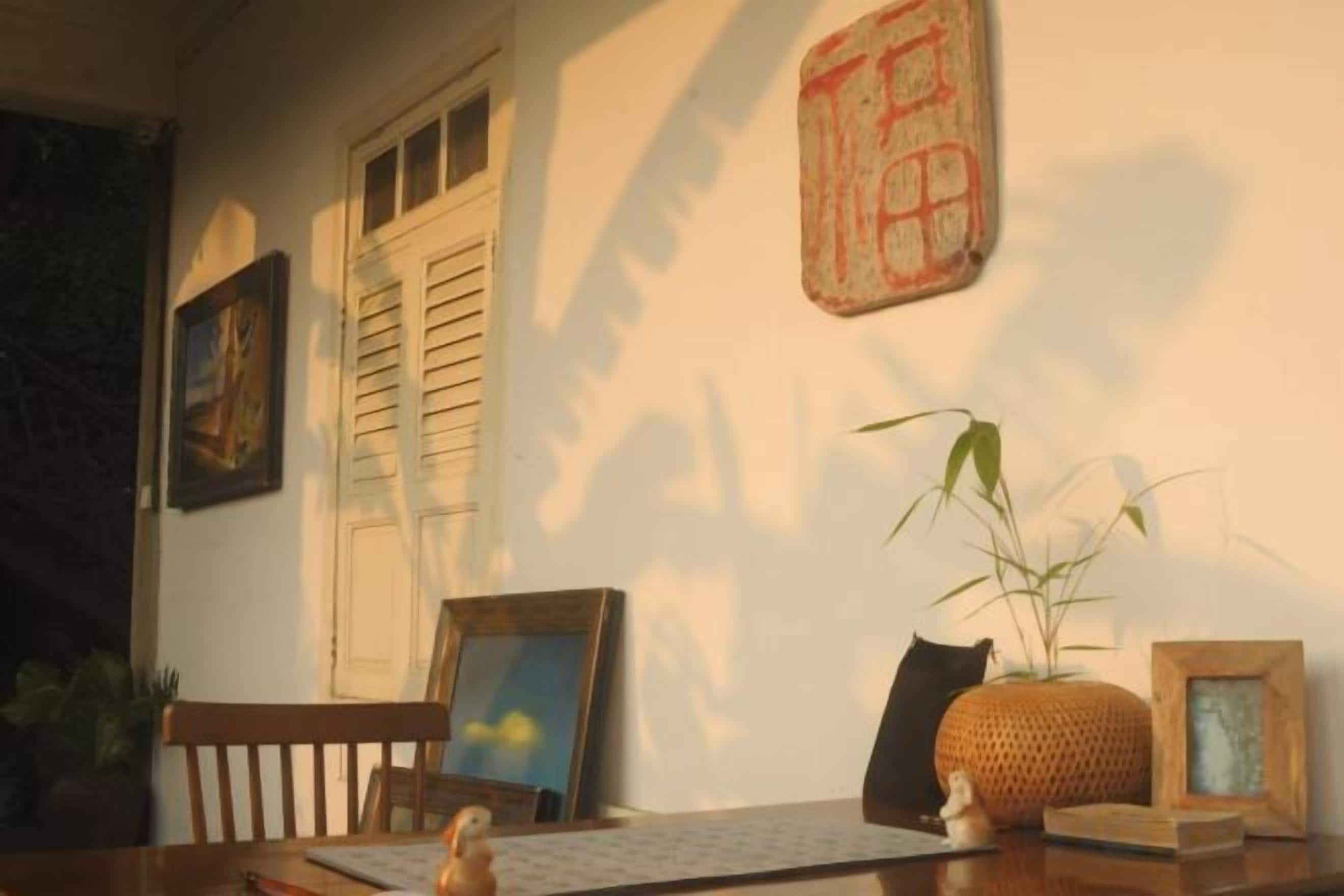 A room with a wooden table, framed pictures, a potted plant, and a wall-mounted decorative piece.