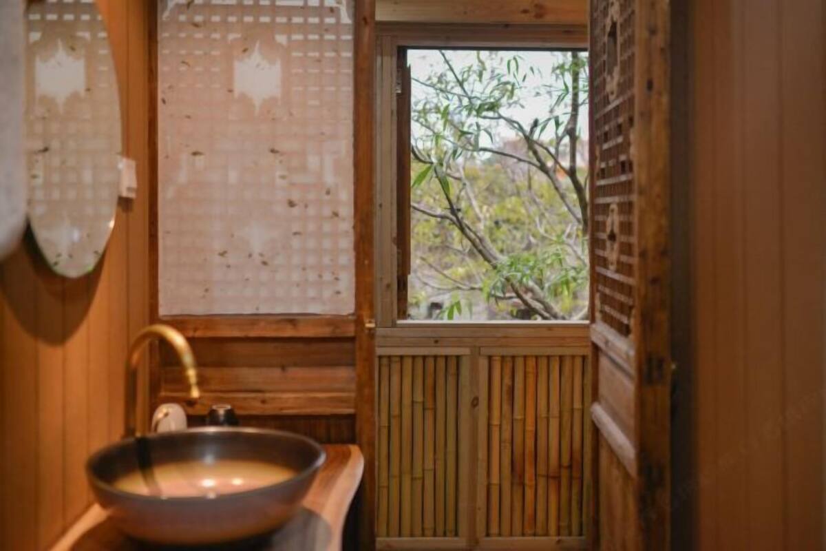 Interior de madera con una ventana, un lavamanos y una puerta de bambú.