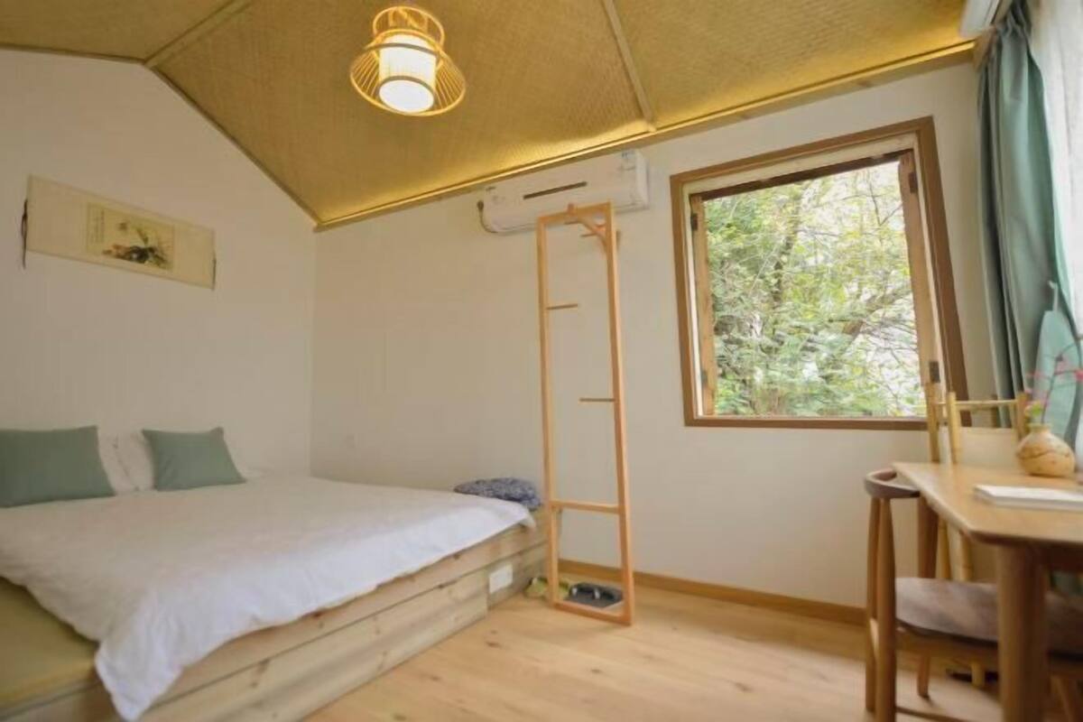 Un dormitorio con una cama, una escalera de madera, un ventanal y una mesa con una silla.