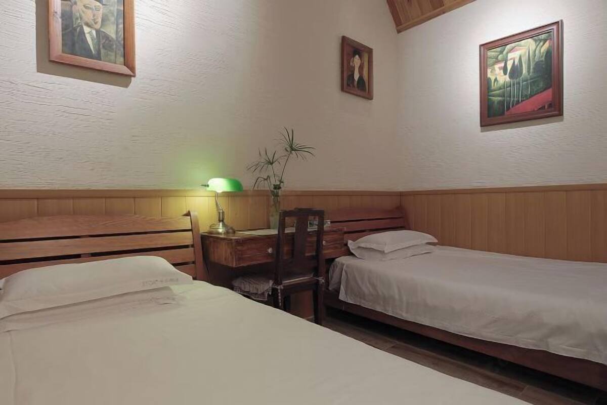Una habitación con dos camas, un escritorio con una silla y una lámpara.