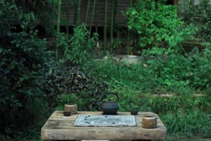 Een houten tafel met een theepot, kopjes en een mat in een tuin.