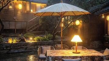 An outdoor dining area with a table and chairs, a large umbrella, and a lamp.