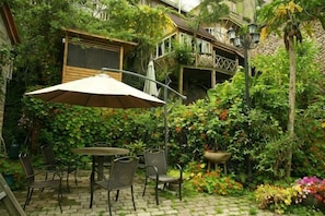 A patio with a table and chairs, surrounded by lush greenery and flowers.