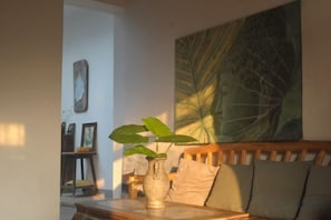Um quarto com um banco de madeira, um vaso com planta e um grande quadro abstrato na parede.