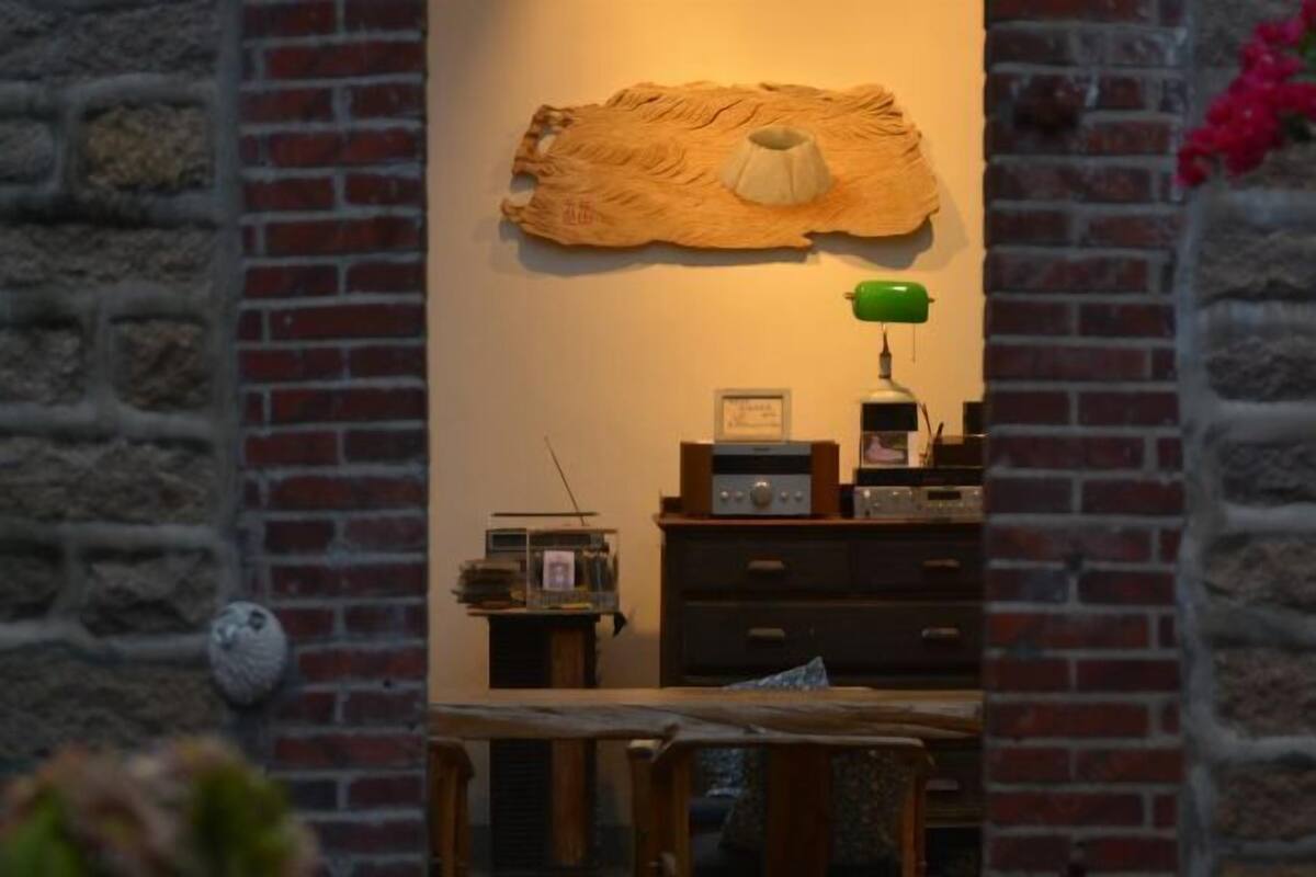 Una habitación con pared de ladrillo, una mesa de madera, una radio y una lámpara verde.