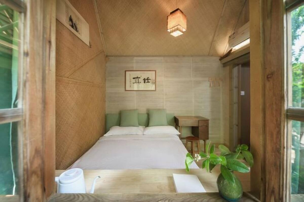 Una habitación pequeña y acogedora con una cama, un escritorio y una silla. Hay un cuadro en la pared y una planta en maceta sobre el escritorio.