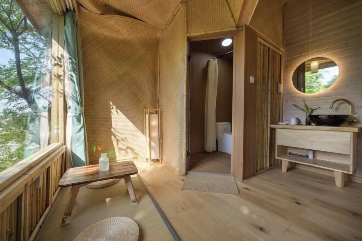Un interior de madera con un banco de madera, un espejo redondo y una pequeña mesa con una botella.