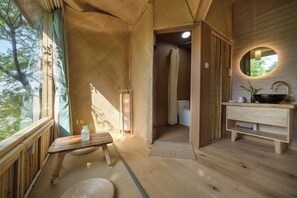 Un intérieur en bois avec un banc en bois, un miroir rond et une petite table sur laquelle se trouve une bouteille.
