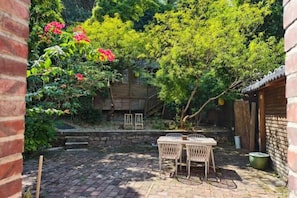 Une terrasse avec une table et des chaises, entourée de verdure et bordée d’un mur de briques.