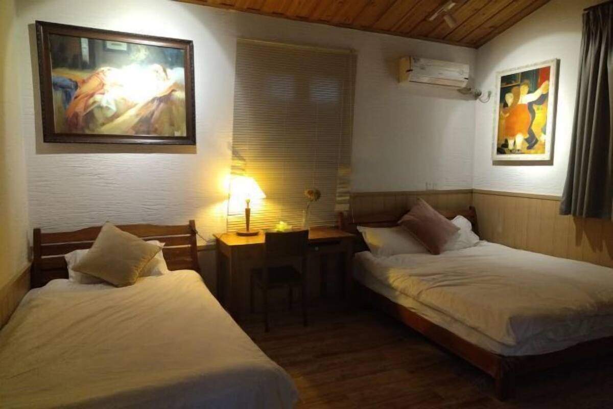 Habitación de hotel con dos camas, un escritorio, una silla y cuadros en las paredes.