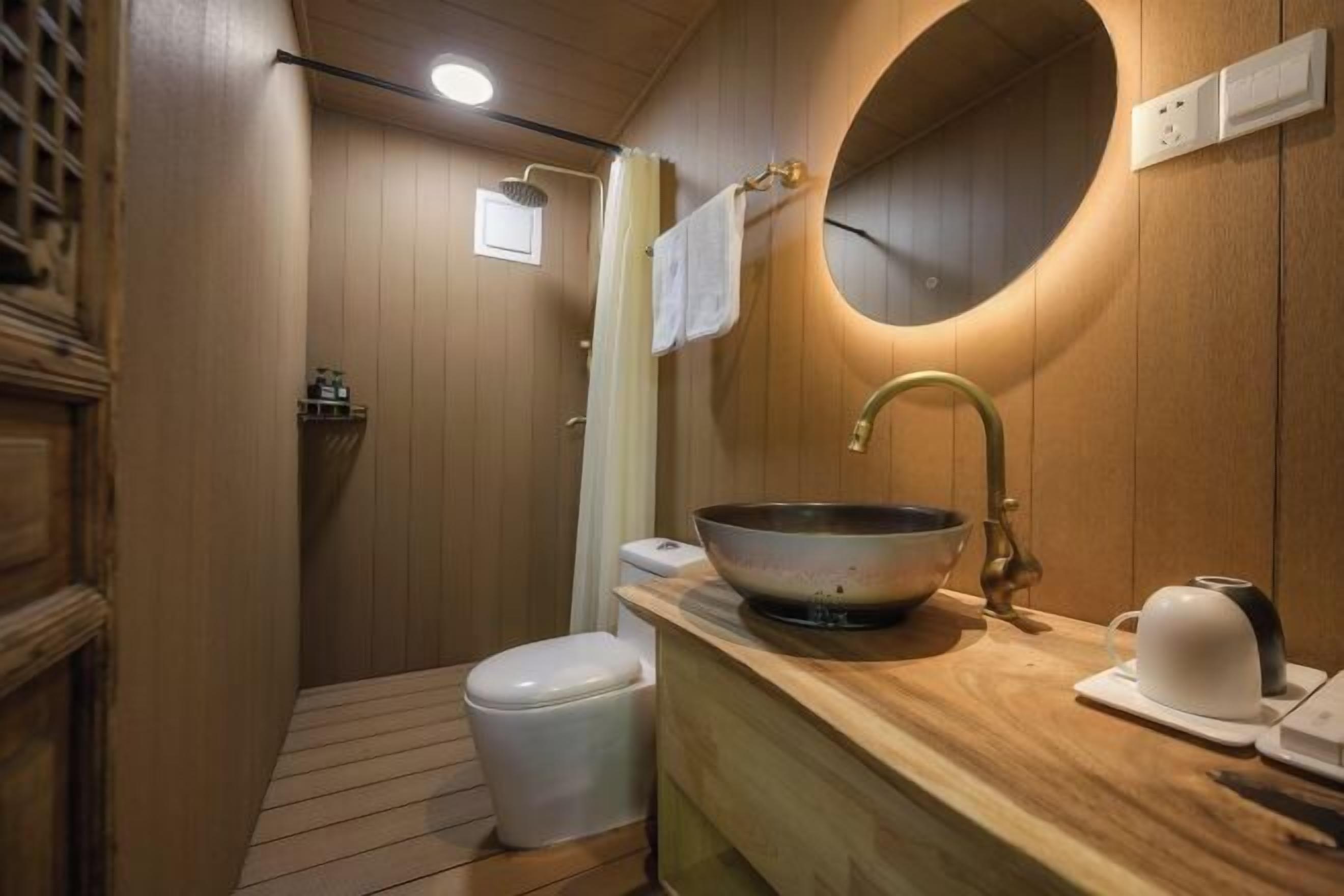 A compact bathroom with a wooden vanity, a large basin, a toilet, and a shower area.