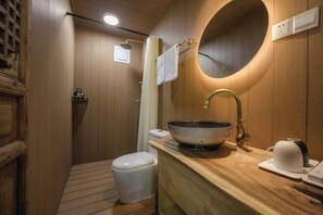 Une salle de bain compacte avec un meuble-lavabo en bois, un grand lavabo, des toilettes et un espace douche.