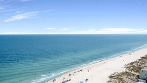 Ein Strand mit klarem, blauem Wasser, sandigem Ufer und einigen Sonnenschirmen.