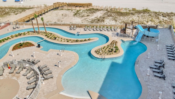 Ein Poolbereich mit mehreren Wasserrutschen und Liegestühlen, angrenzend an einen Sandstrand.