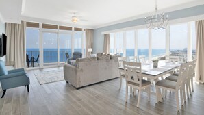 Ein geräumiges Wohnzimmer mit einer großen Couch, einem Esstisch und Stühlen. Ein Balkon bietet Blick aufs Meer.