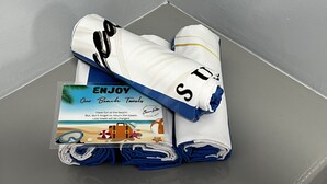 A neatly folded towel with a beach-themed towel bag and a printed towel bag with a beach scene and text.
