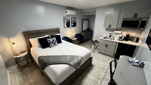 A modern bedroom with a large bed, bedside tables, a desk, and a kitchenette.