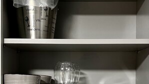 A kitchen shelf with a stainless steel wine bucket, clear glassware, bowls, plates, a tray, and white mugs.