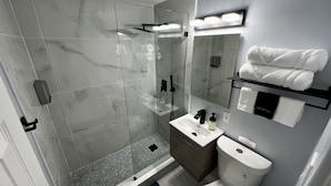 A modern bathroom with a glass shower enclosure, a vanity with a sink and mirror, and a towel rack with neatly folded towels.