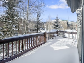 A snow-covered deck with a wooden railing, a table, and chairs.