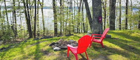 A lakeside setting with two red chairs and a birdhouse near a tree.