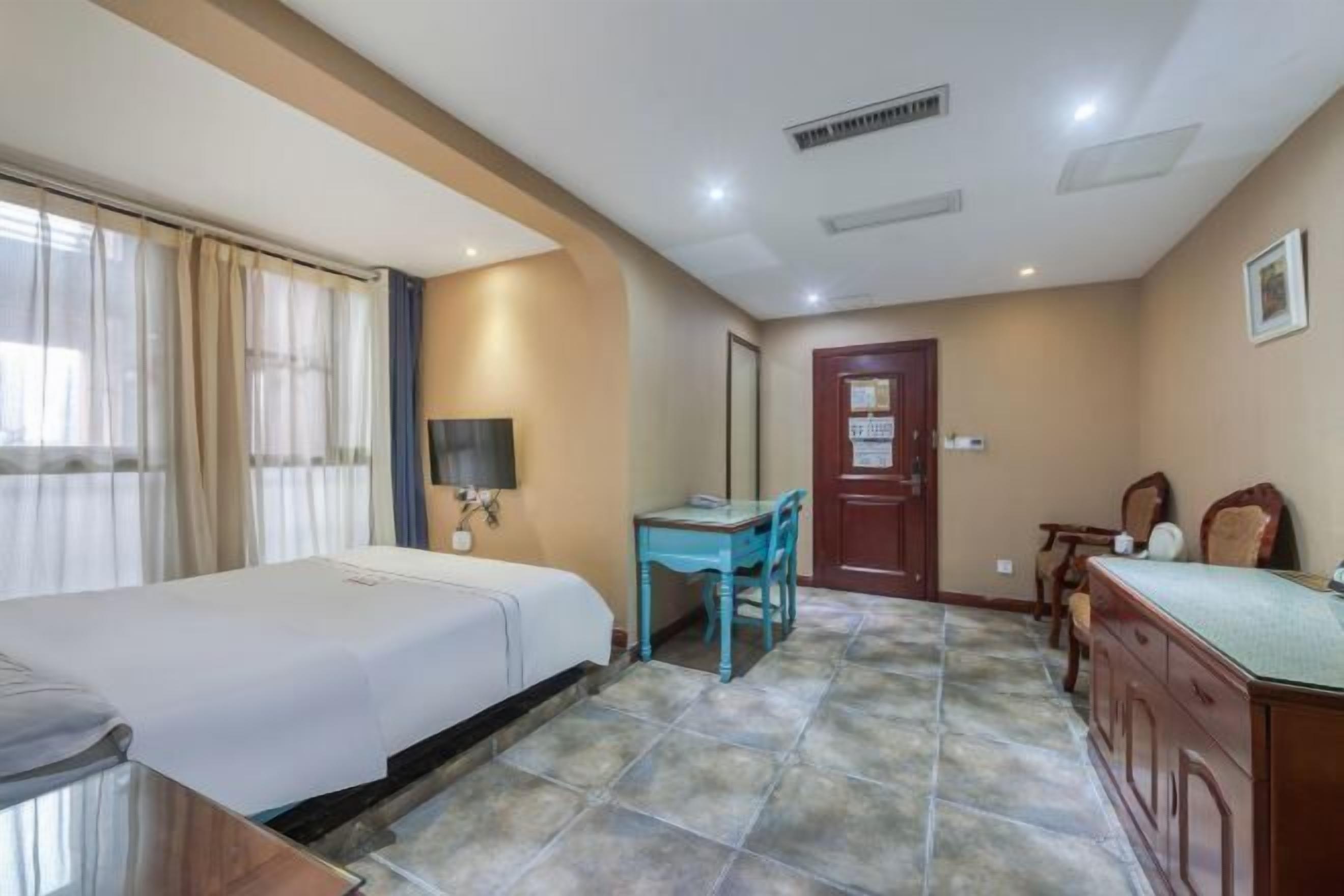 A hotel room with a bed, a desk, a chair, a dresser, and a door with a sign.