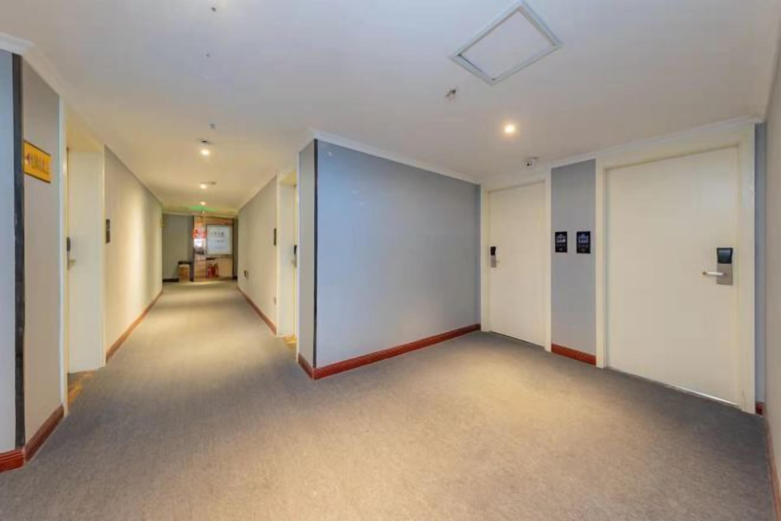 Un couloir d’hôtel avec des revêtements de sol en moquette, des murs blancs et des portes portant les numéros des chambres.