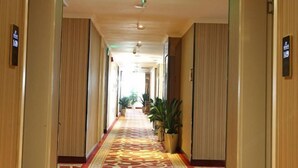 Un pasillo de hotel con alfombra estampada, plantas en macetas e iluminación verde en el techo.