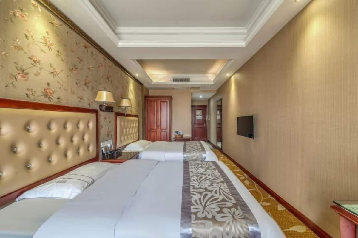 Una habitación de hotel con una cama grande, cabecero, mesita de noche, lámpara y televisor.