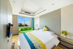 Une chambre d’hôtel avec un grand lit, un canapé vert, une télévision et une fenêtre donnant sur la ville.