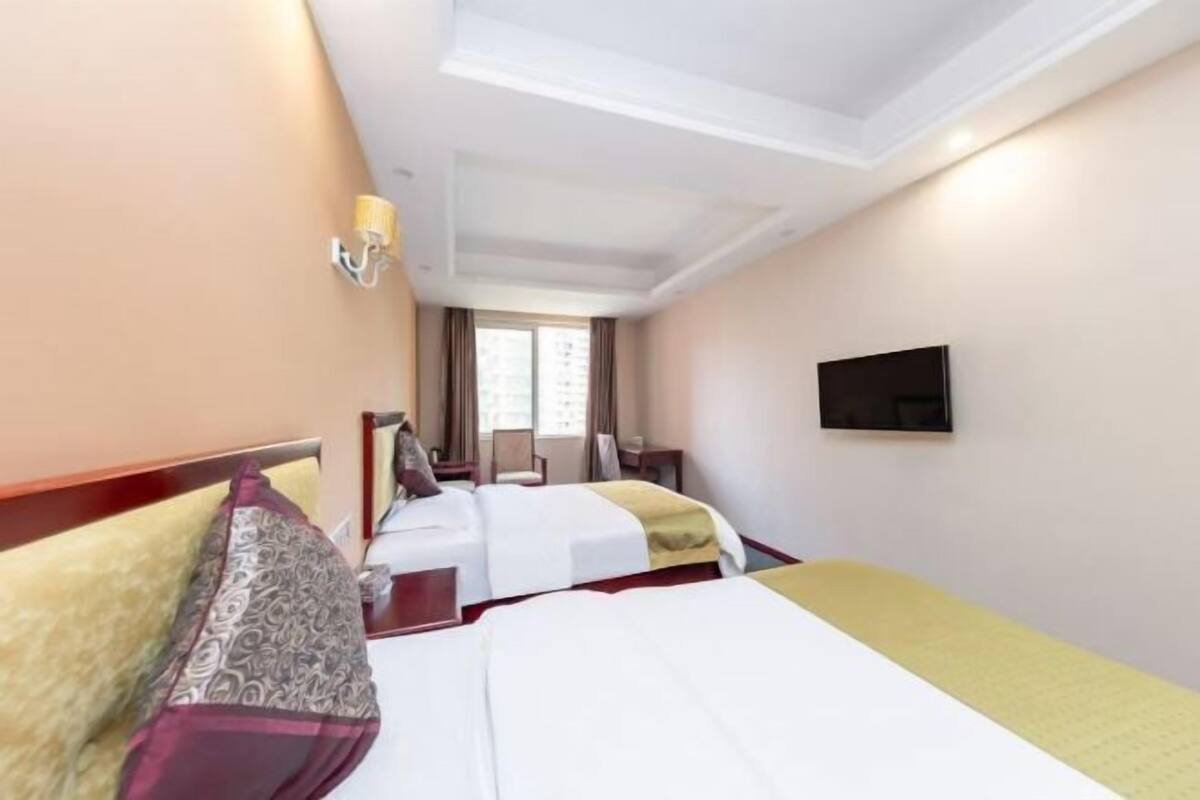 Una habitación de hotel con dos camas, televisión, ventana y lámpara.