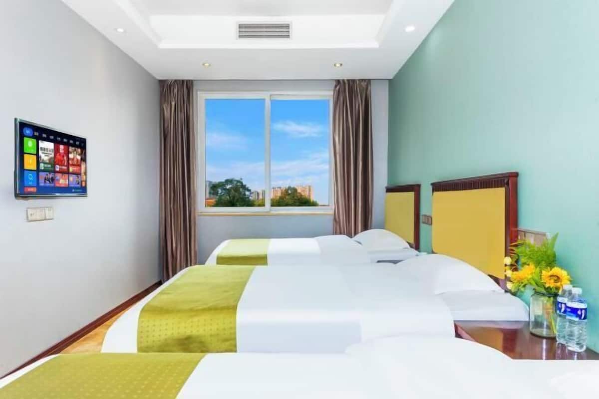 Una habitación de hotel con un ventanal grande, un televisor de pantalla plana, un escritorio con un florero y dos camas.