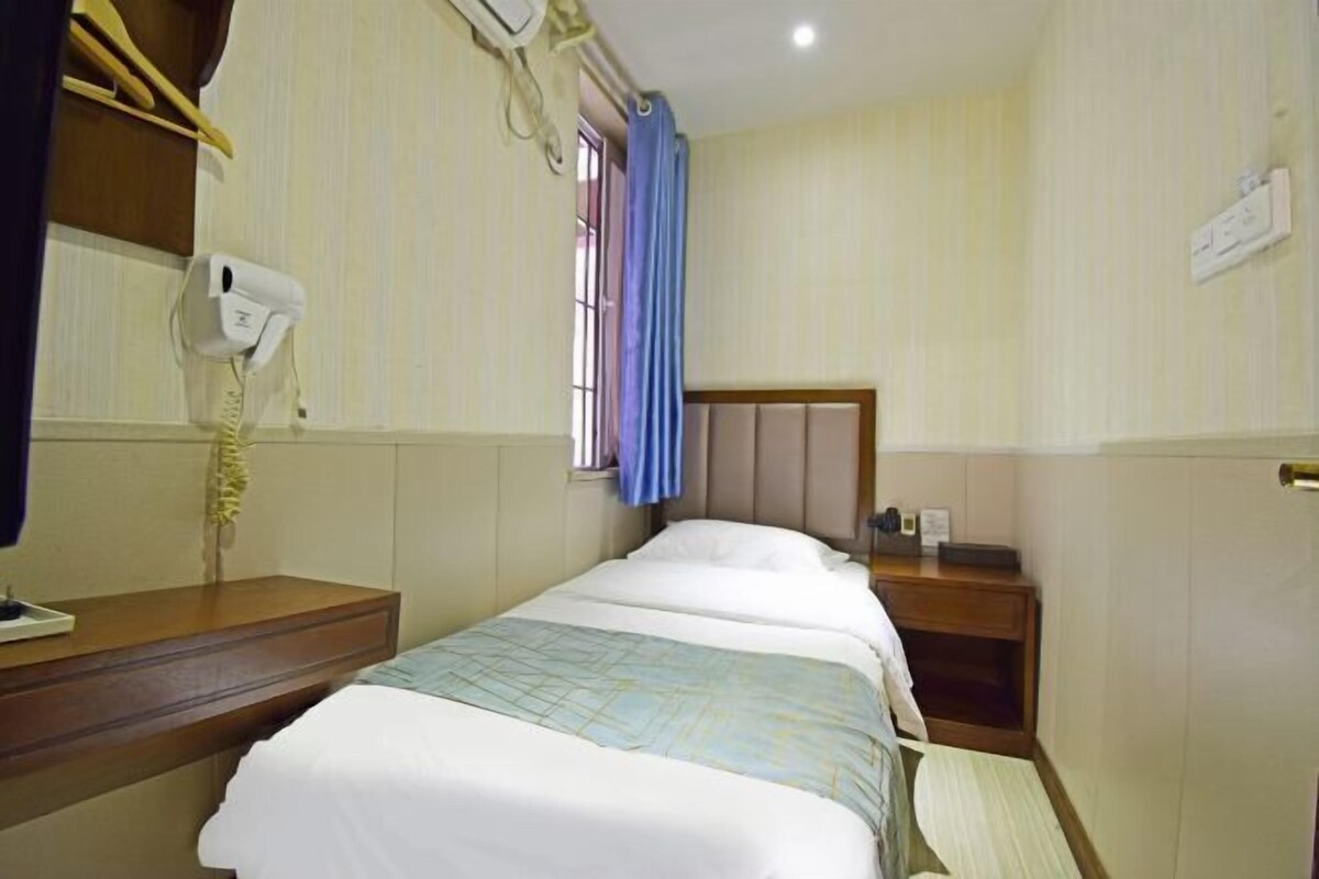 Une chambre d’hôtel avec deux lits simples, une commode en bois, une table de chevet avec une lampe, un sèche-cheveux et une fenêtre avec des rideaux bleus.