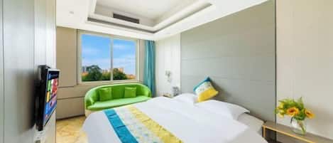 A hotel room with a large bed, a green armchair, a TV, and a window with a city view.